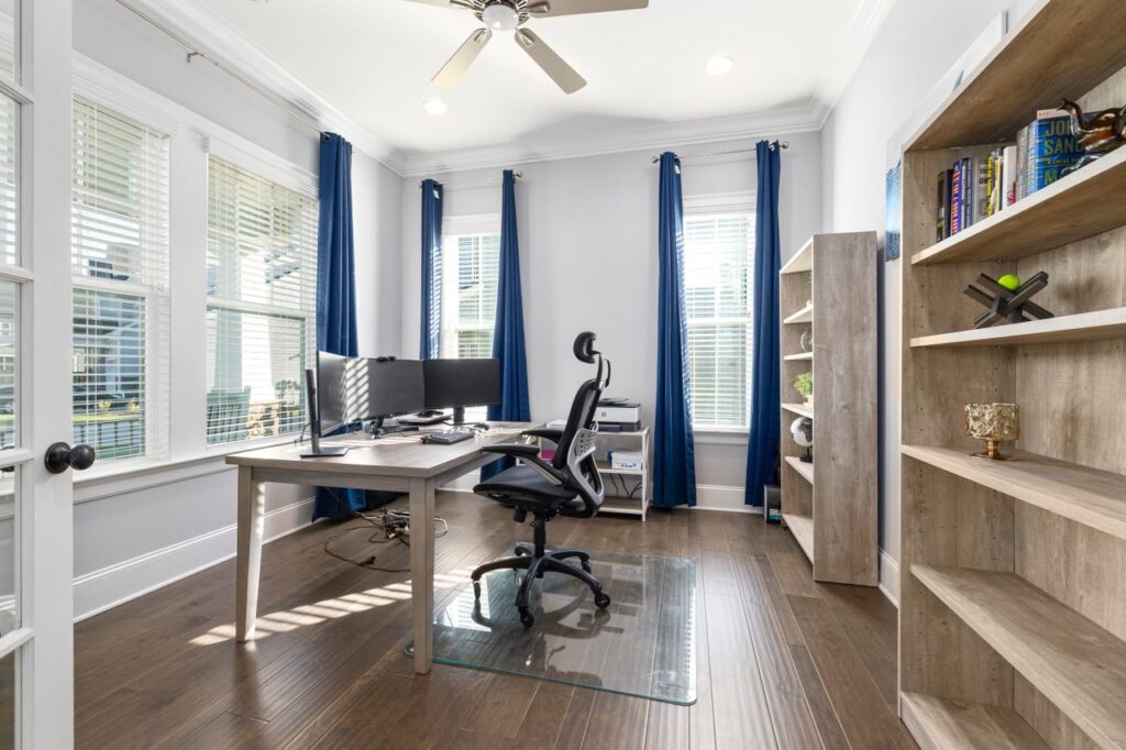 A bright modern home office featuring a desk, computer, and bookshelves with ample natural light.